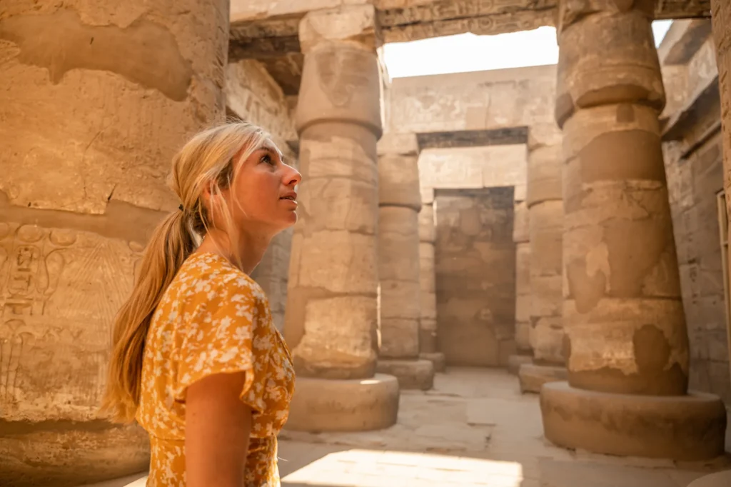 Woman looking up in awe among the massive carved columns of Karnak Temple in Luxor, Egypt, with hieroglyphs visible on the walls.