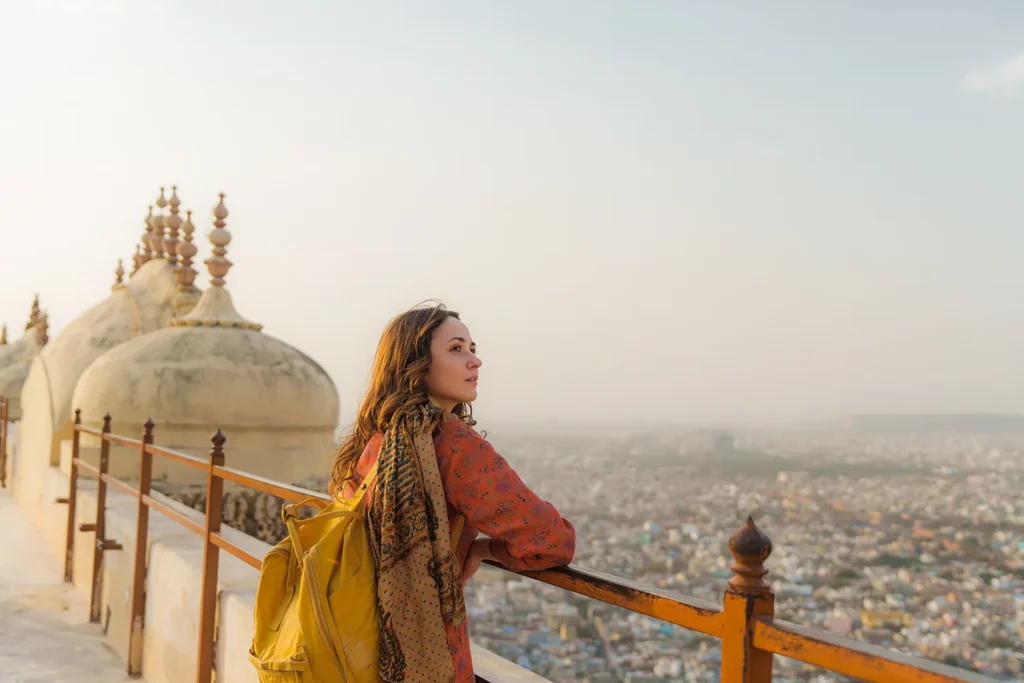 A woman pauses at a fort railing above Jaipur, looking out over the city with quiet reflection